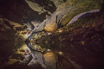 Hang En Cave: Im See vor dem gewaltigen Boulderhaufen spiegeln sich drei Lichter, in dessen Schein man unsere drei Beleuchter als schwarze Umrisse erkennen kann.
