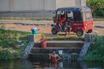 Polonnaruwa: Alltagsszene am Fluss in der Stadt: Mama hat Waschtag und putzt Zähne, während Papa und Sohn "a nice day" wünschen.