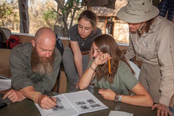 Bruce erklärt Sophie, Martina und Kim anhand von Fotos, wo sich bei verschiedenen Tieren das Gehirn befindet. Im Falle eines Angriffs  muss der Schütze es mit seinem ersten Schuss treffen.