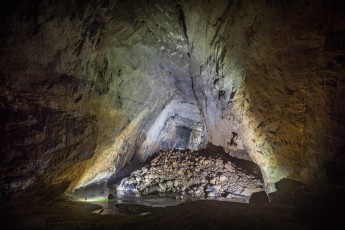 View through the middle room of the Hang En Cave. Here the light of our cave lamps mingles with the daylight that flows in through the exit of the cave. The Hang En Cave is huge already : On the top of the boulder pile one can identify the green jersey of an expedition member in front of a dark square in the background.