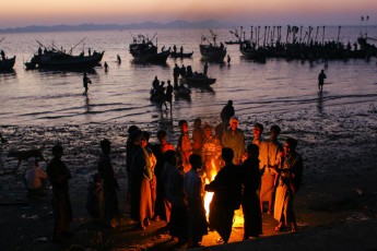 Burma/Myanmar: Die ganze Nacht waren die Männer draußen beim Fischen. Jetzt, in der Morgendämmerung, wärmen sie sich kurz am Feuer auf. Gleich müssen sie ihren Fang noch auf dem Markt von Sittwe bringen und dort verkaufen. Ein Knochenjob.