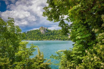 The turquoise waters of Lake Bled shimmer through the canopy of chestnut and lime trees, while above, the medieval castle sits enthroned on its 139-metre-high rock like a fairytale castle from a bygone era.