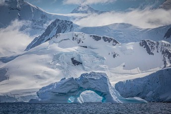 Ein gewaltiger Eisbogen rahmt den Blick auf die dahinterliegenden Gletscher. Wellen und Schmelzwasser haben dieses Tor geschaffen – ein vergängliches Kunstwerk vor unvergänglichen, schneebedeckte Gipfeln.